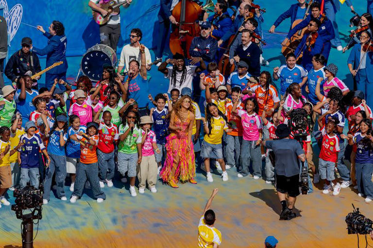 Shakira performing live on stage surrounded by diverse children singing at the FIFA World Cup celebration